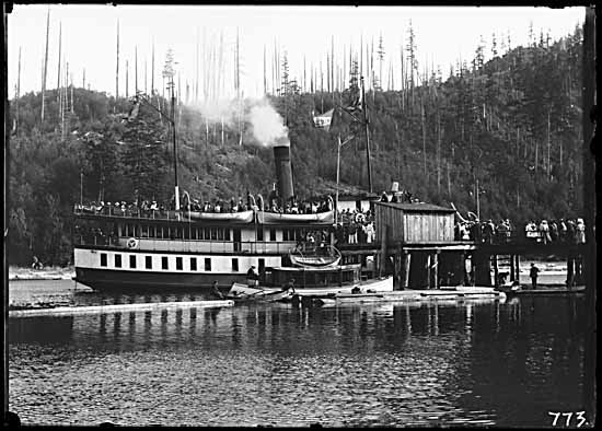 Terminal Steam Navigation Co. vessel alongside the pier at Bowen Island. Many people on board and on the pier. Smaller boat in foreground. Photographer/Studio:Philip Timms (VPL #2881)